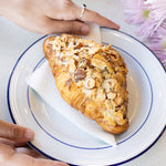 Pastry on a plate with hands holding it, surrounded by flowers and more pastries.