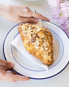 Pastry on a plate with hands holding it, surrounded by flowers and more pastries.