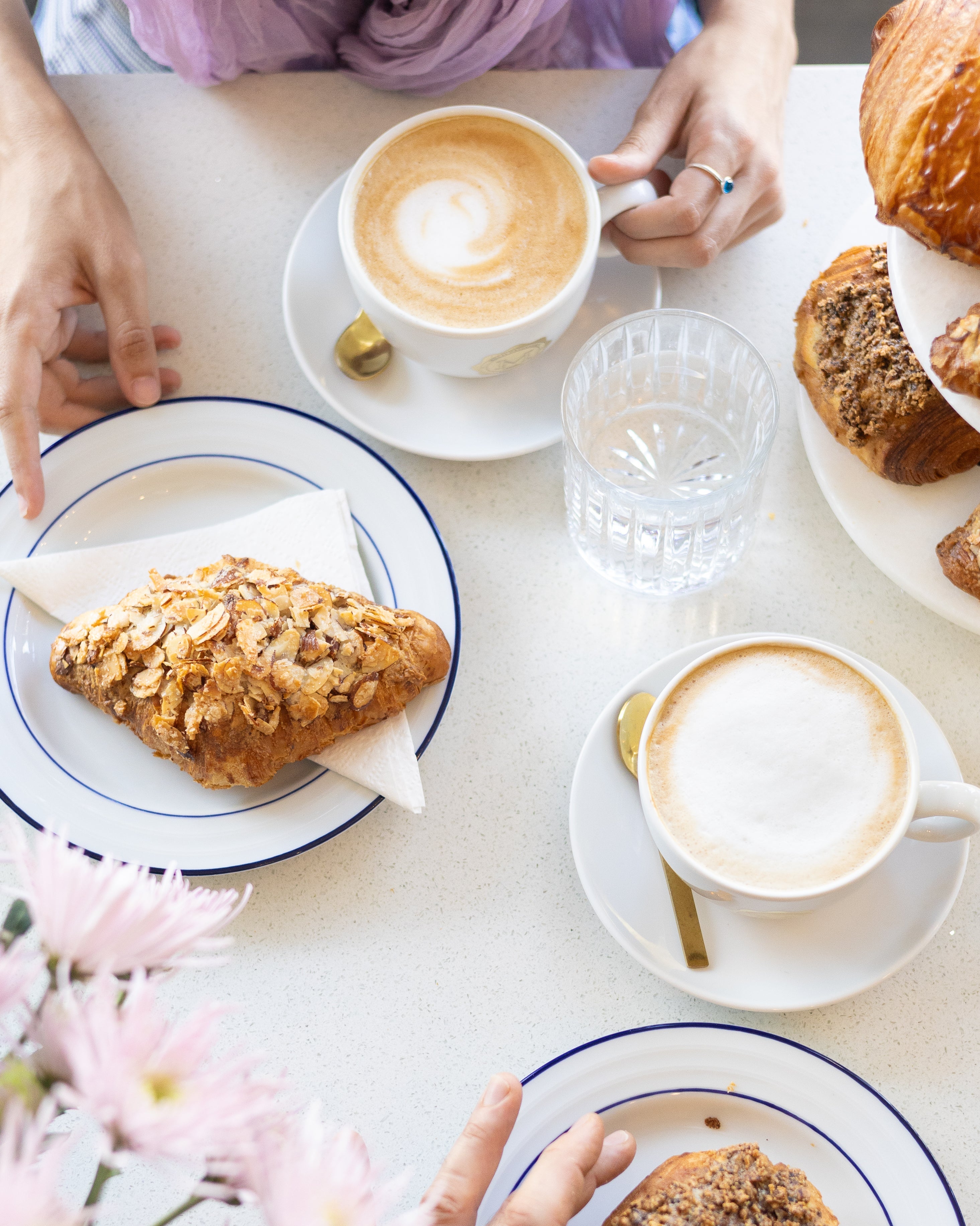 People enjoying pastries and coffee at a table with flowers.