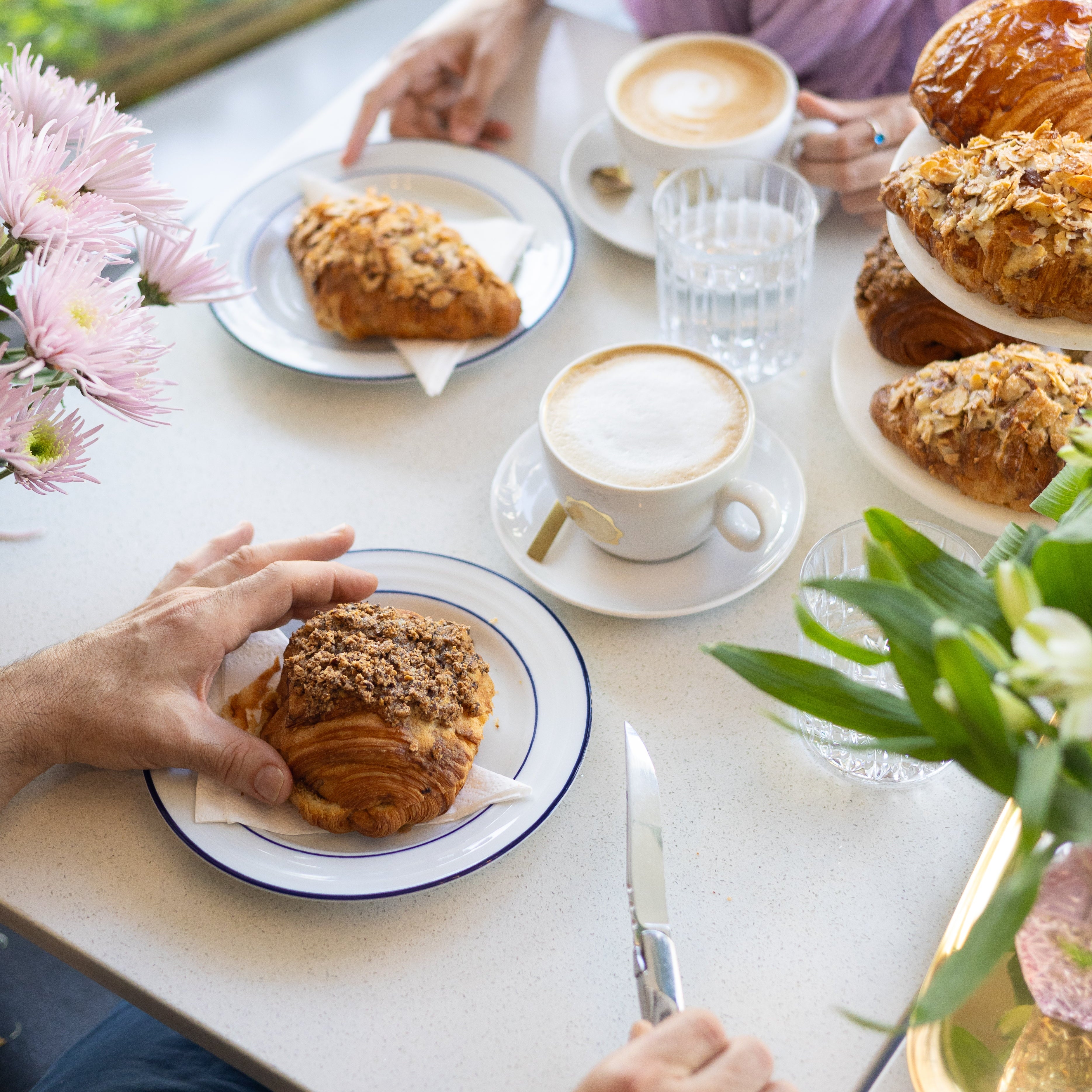 Two people enjoying pastries and coffee at a table with flowers and a window view.