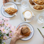 People enjoying pastries and coffee at a table with flowers and cutlery.