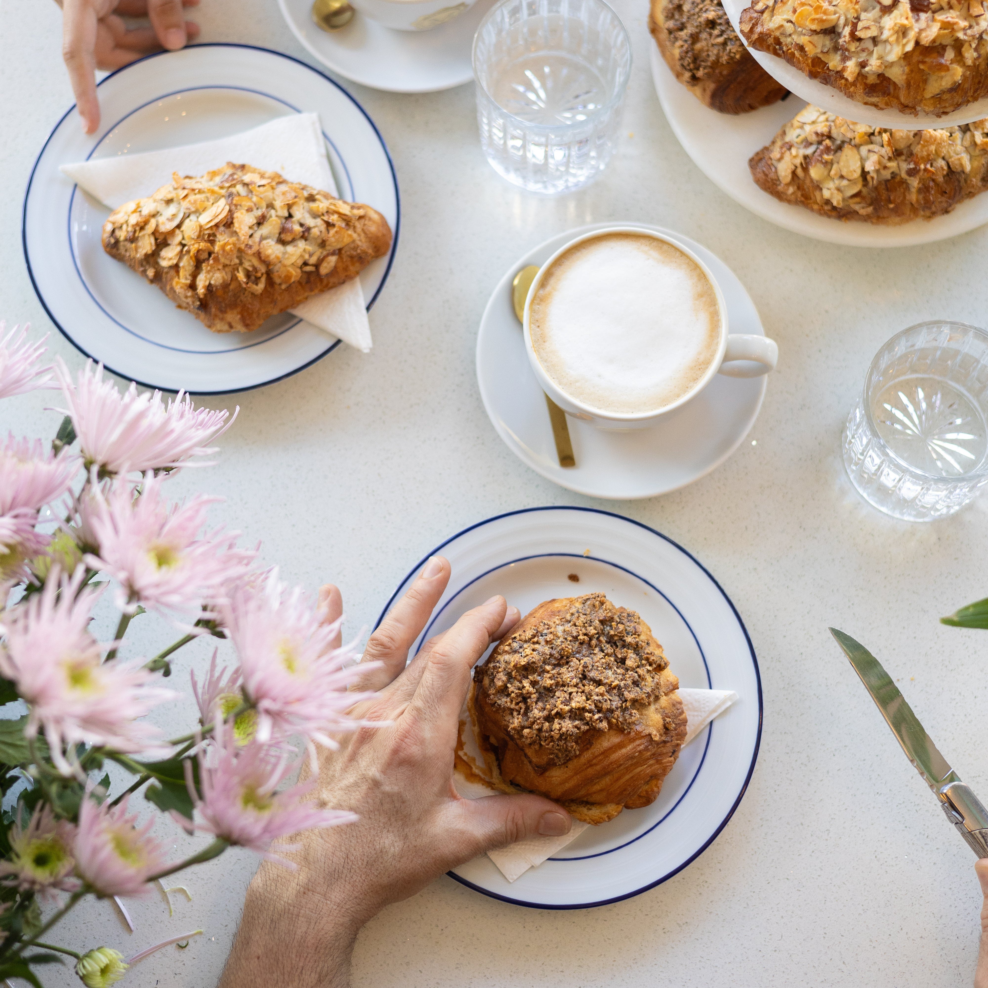 People enjoying pastries and coffee at a table with flowers and cutlery.