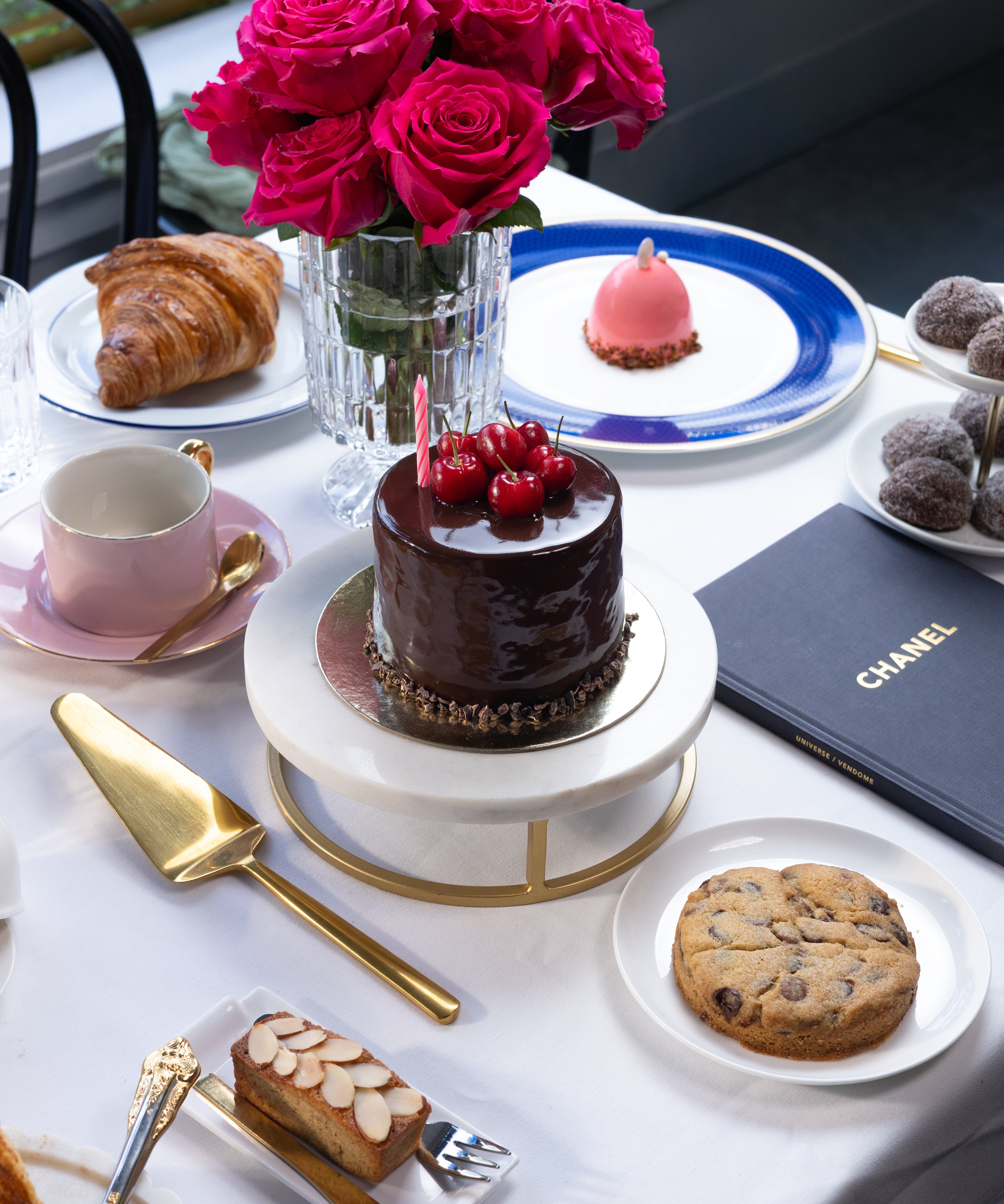 Table setting with a chocolate cake, cookies, and flowers on a white tablecloth.