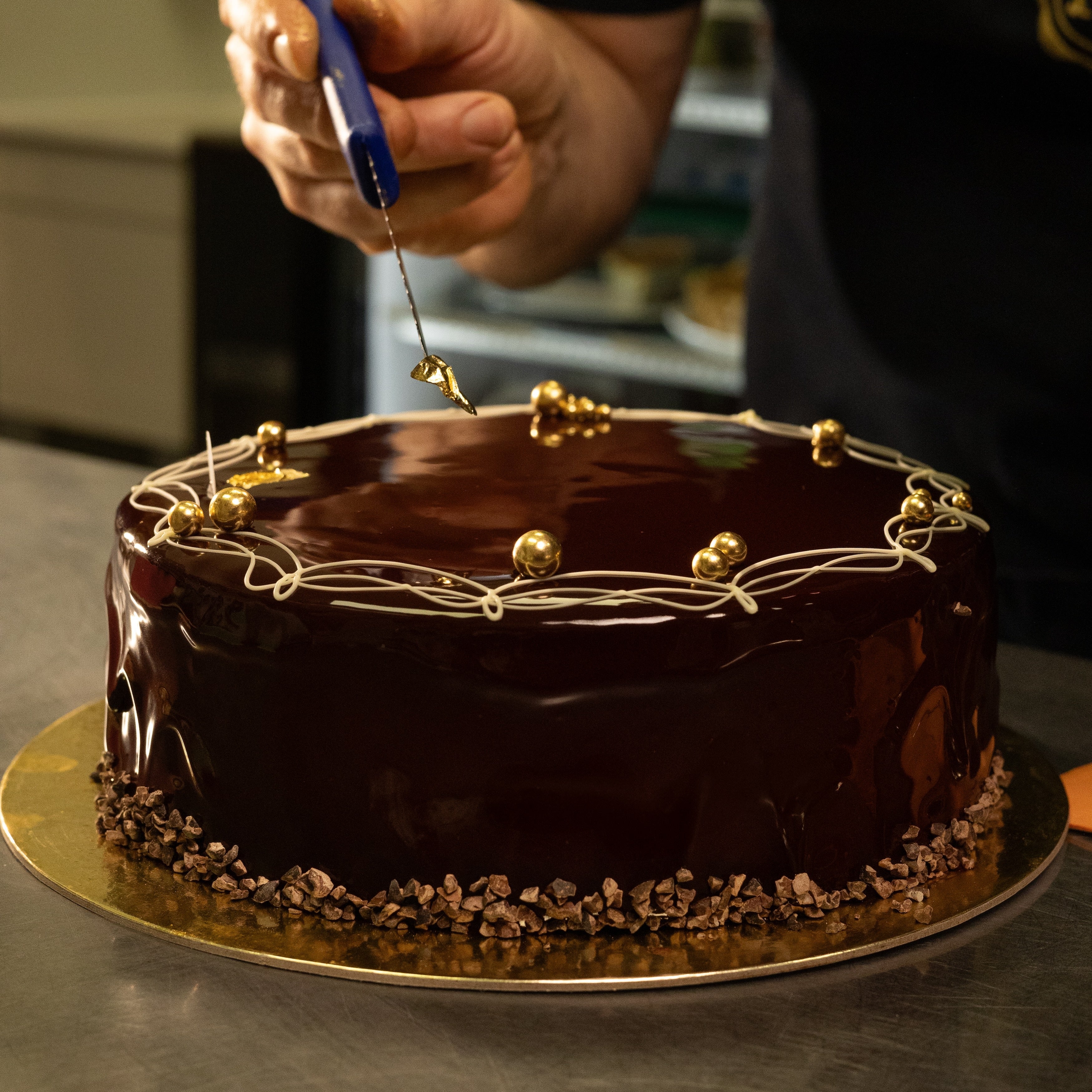 Chocolate cake with gold decorations being prepared on a metal tray.