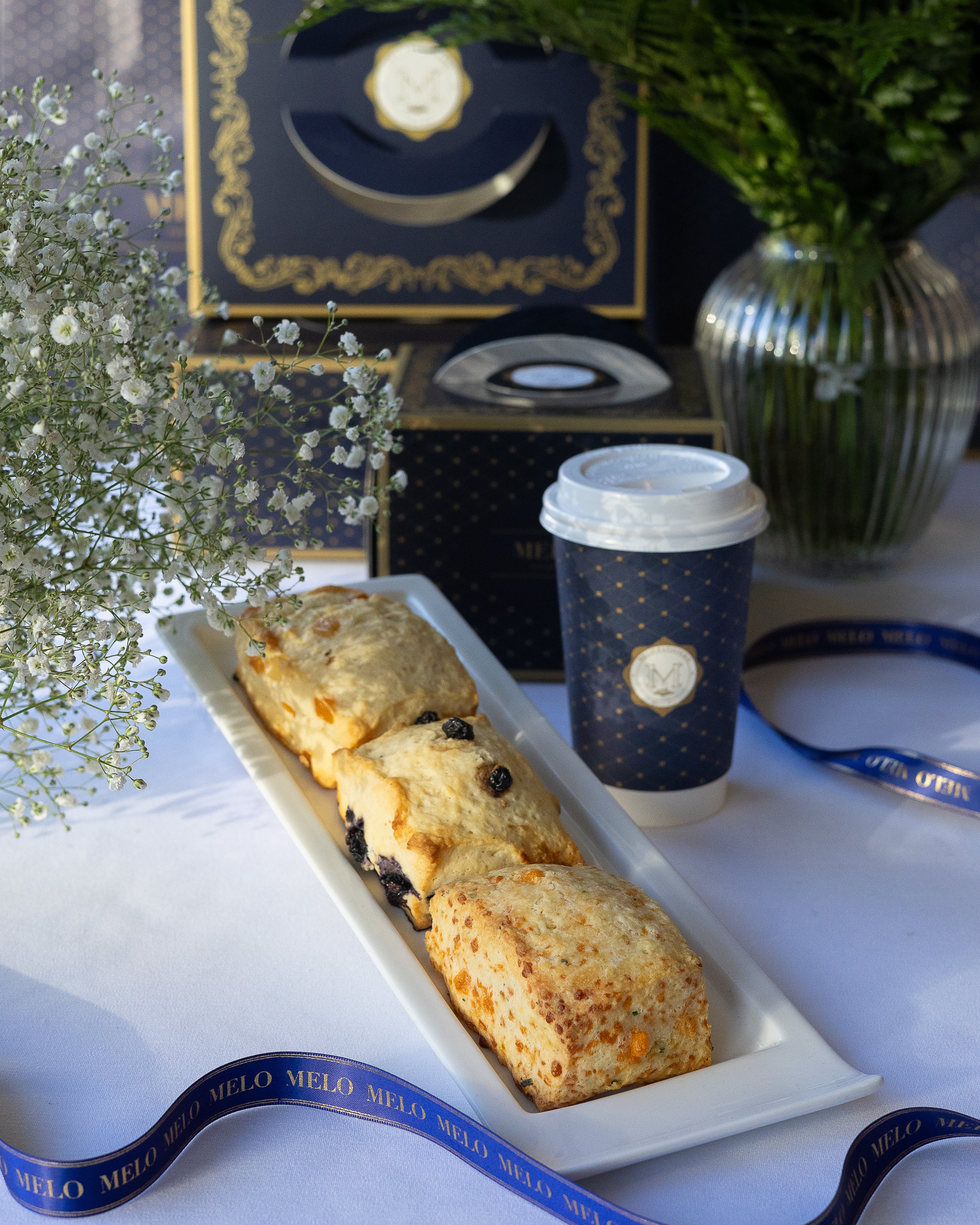Three scones on a tray with a coffee cup featuring a logo, set against a decorative background.