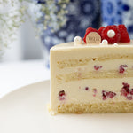 Slice of layered cake with berries and cream on a white plate, with a blurred floral background.
