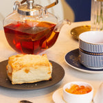 Tea set with a teapot, cup, and plate of cake on a table.