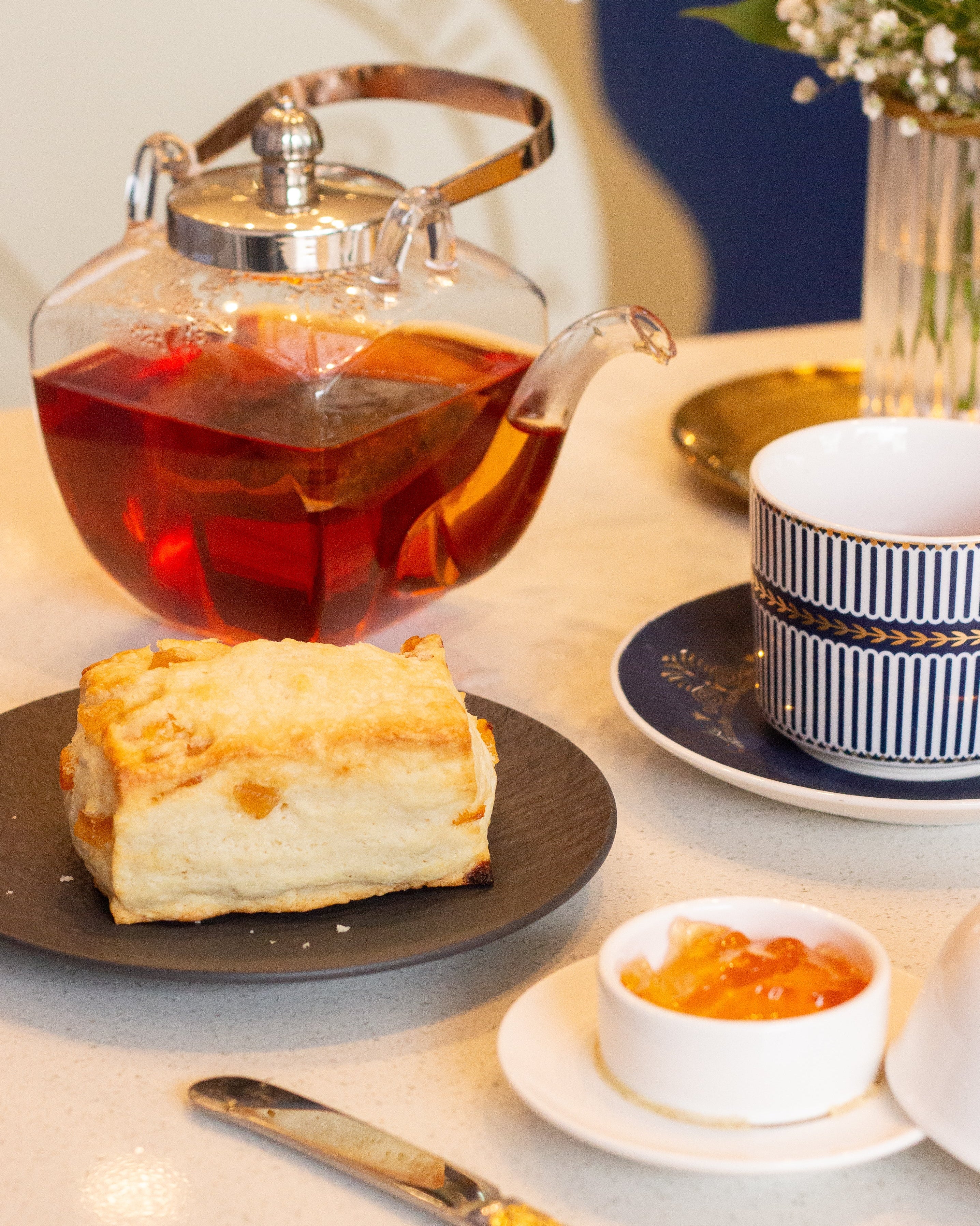 Tea set with a teapot, cup, and plate of cake on a table.