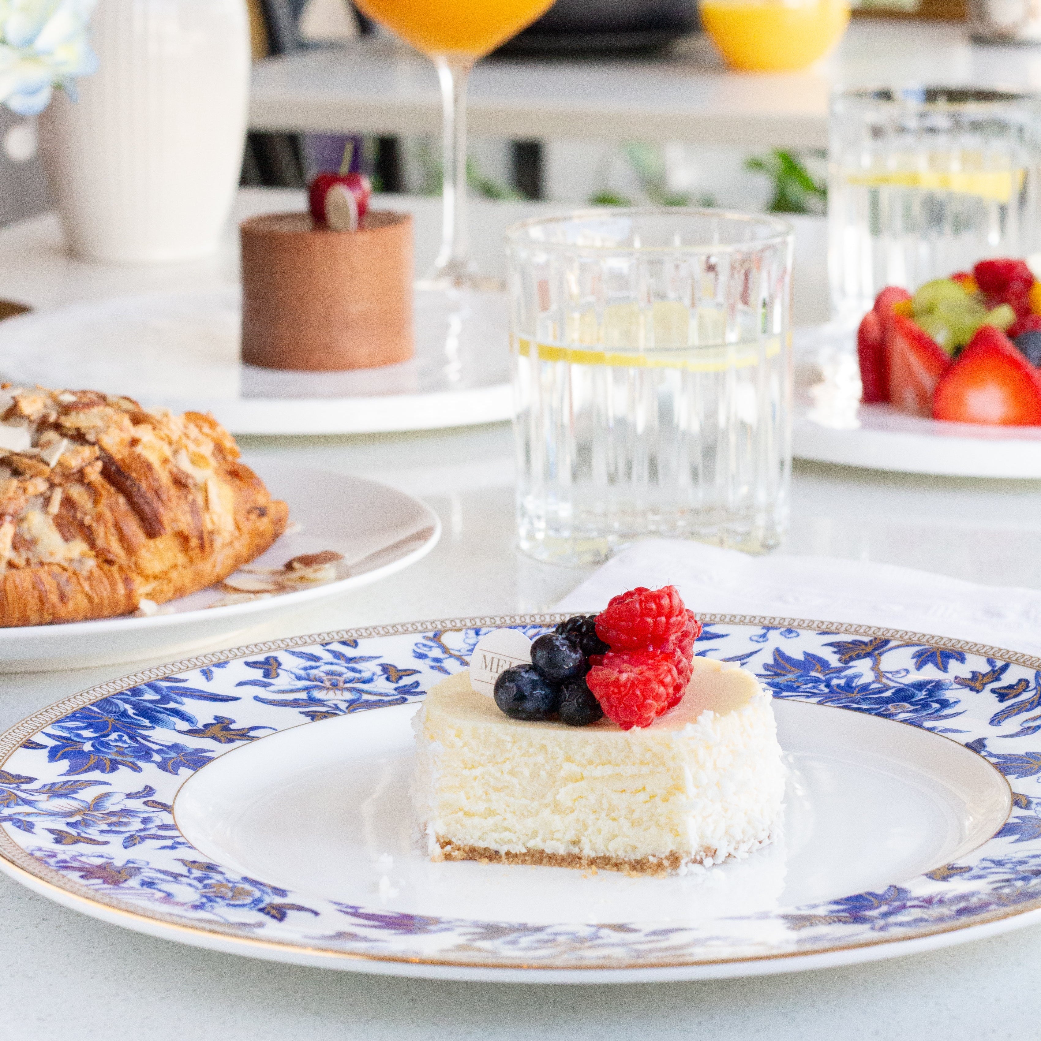 Table setting with a slice of cheesecake, berries, and a glass of orange juice.