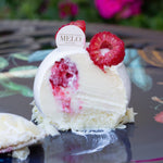 Slice of white cake with red berries on a black plate with flowers in the background