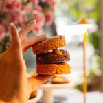 Hand holding a stack of small, round, brown pastries with a blurred floral background