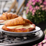 Croissant sandwich with cheese and ham on a plate outdoors with flowers in the background