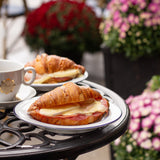 Two croissants with fillings on a plate with a cup of coffee, set on a table outdoors with flowers in the background.
