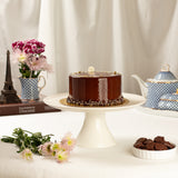 Chocolate cake on a white stand with flowers and teapots in the background