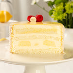 Layered cake with lemon filling on a white plate, garnished with raspberries and a lemon slice.