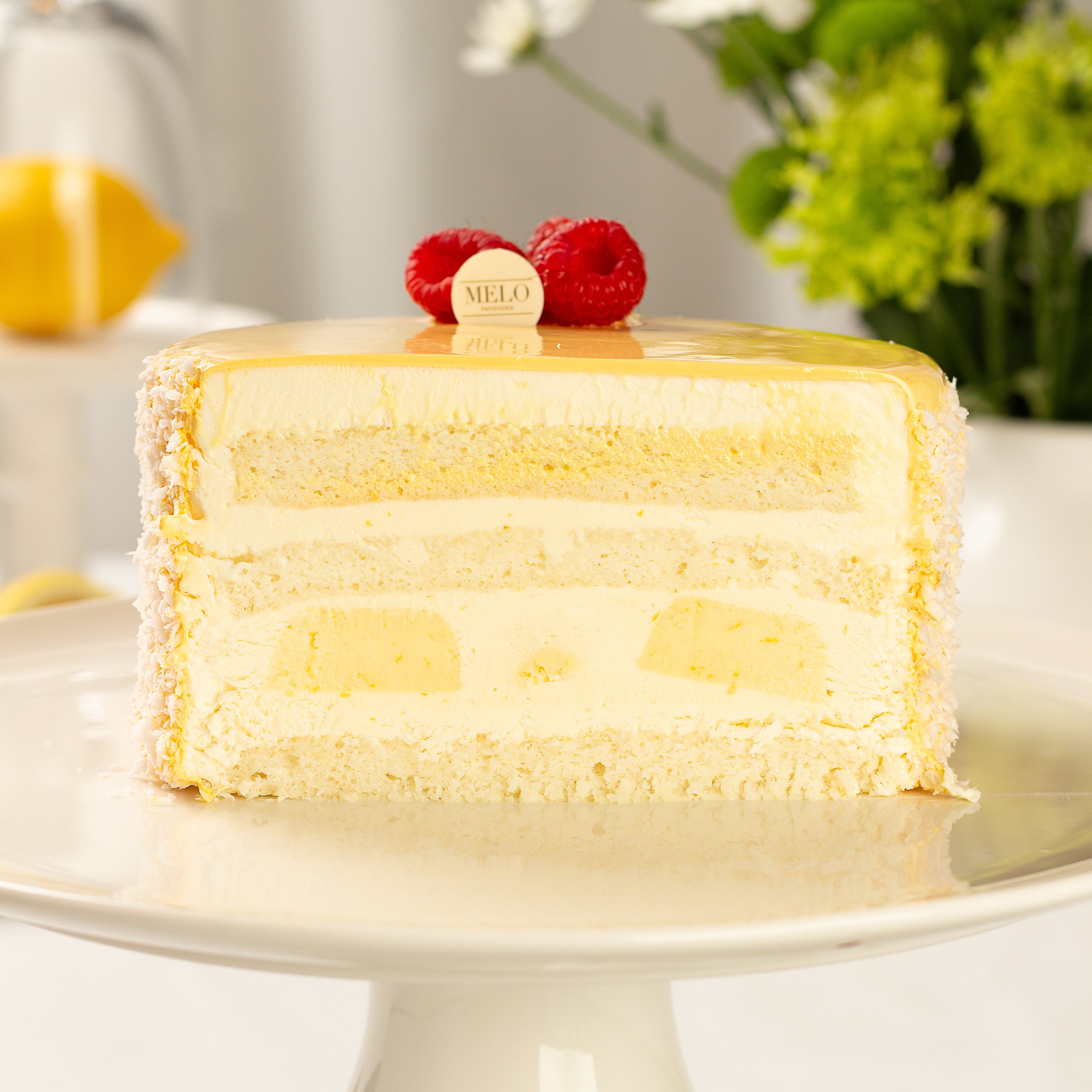 Layered cake with lemon filling on a white plate, garnished with raspberries and a lemon slice.
