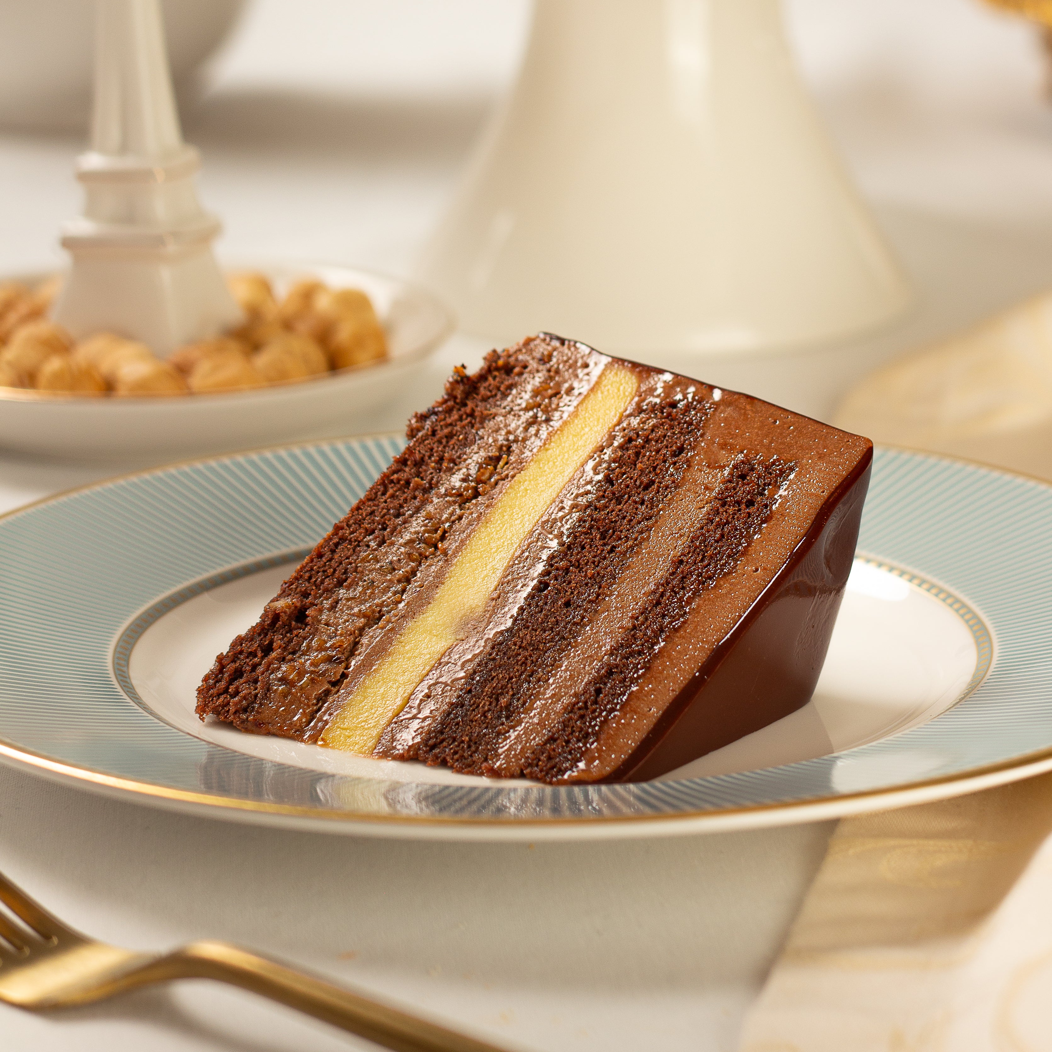 Slice of layered chocolate cake on a decorative plate with a blurred background