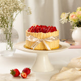 Decorative cake with strawberries on a white stand, surrounded by flowers and a vase.
