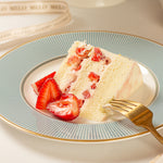 Slice of strawberry cake on a decorative plate with a gold fork.
