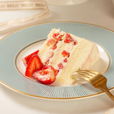 Slice of strawberry cake on a decorative plate with a gold fork.
