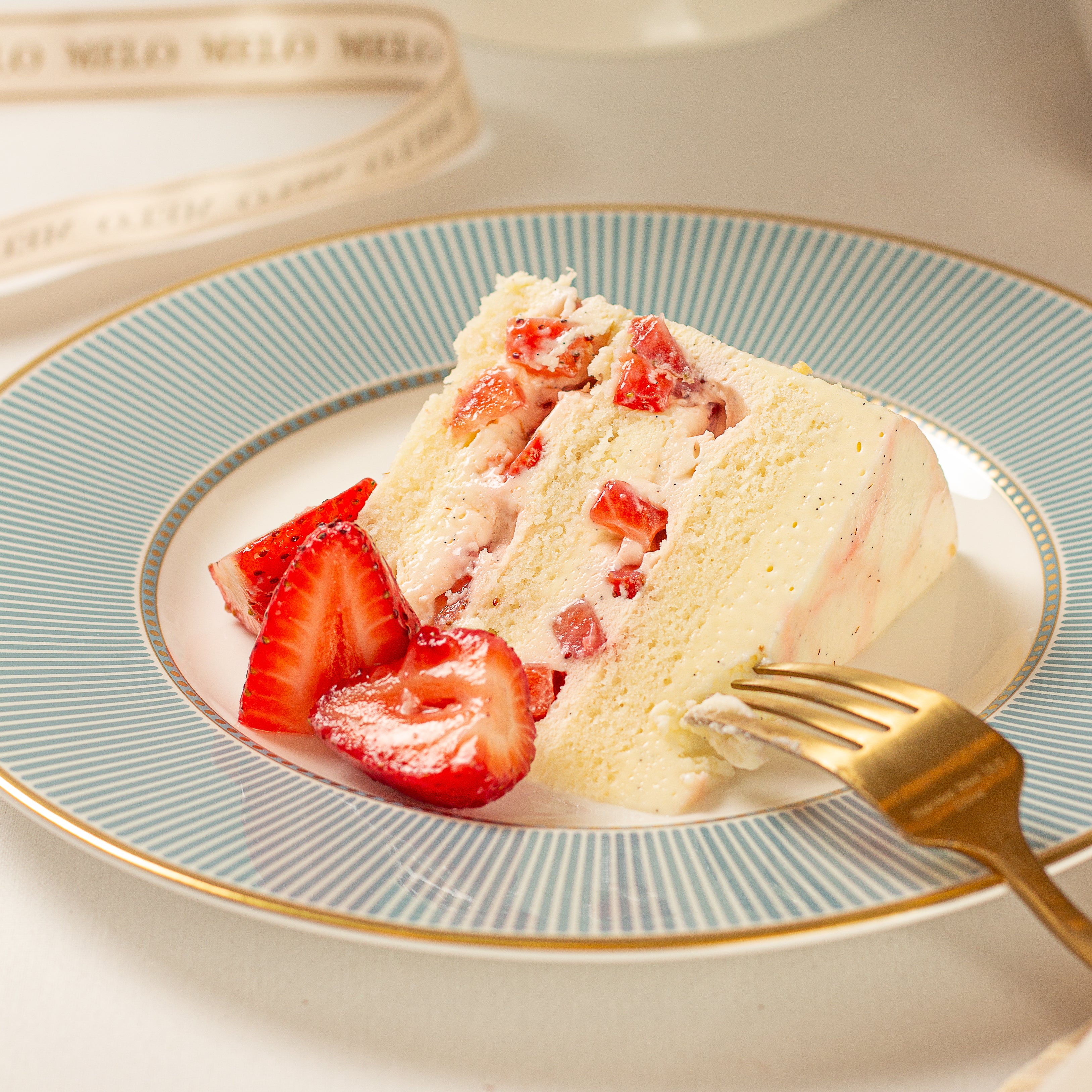 Slice of strawberry cake on a decorative plate with a gold fork.