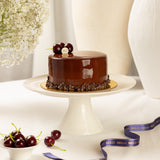 Chocolate cake on a white stand with cherries and MELO ribbon in the background