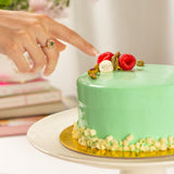 Green cake with berries and a hand pointing at it, with books in the background