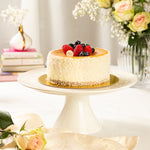 Cheesecake with berries on a white cake stand with flowers in the background
