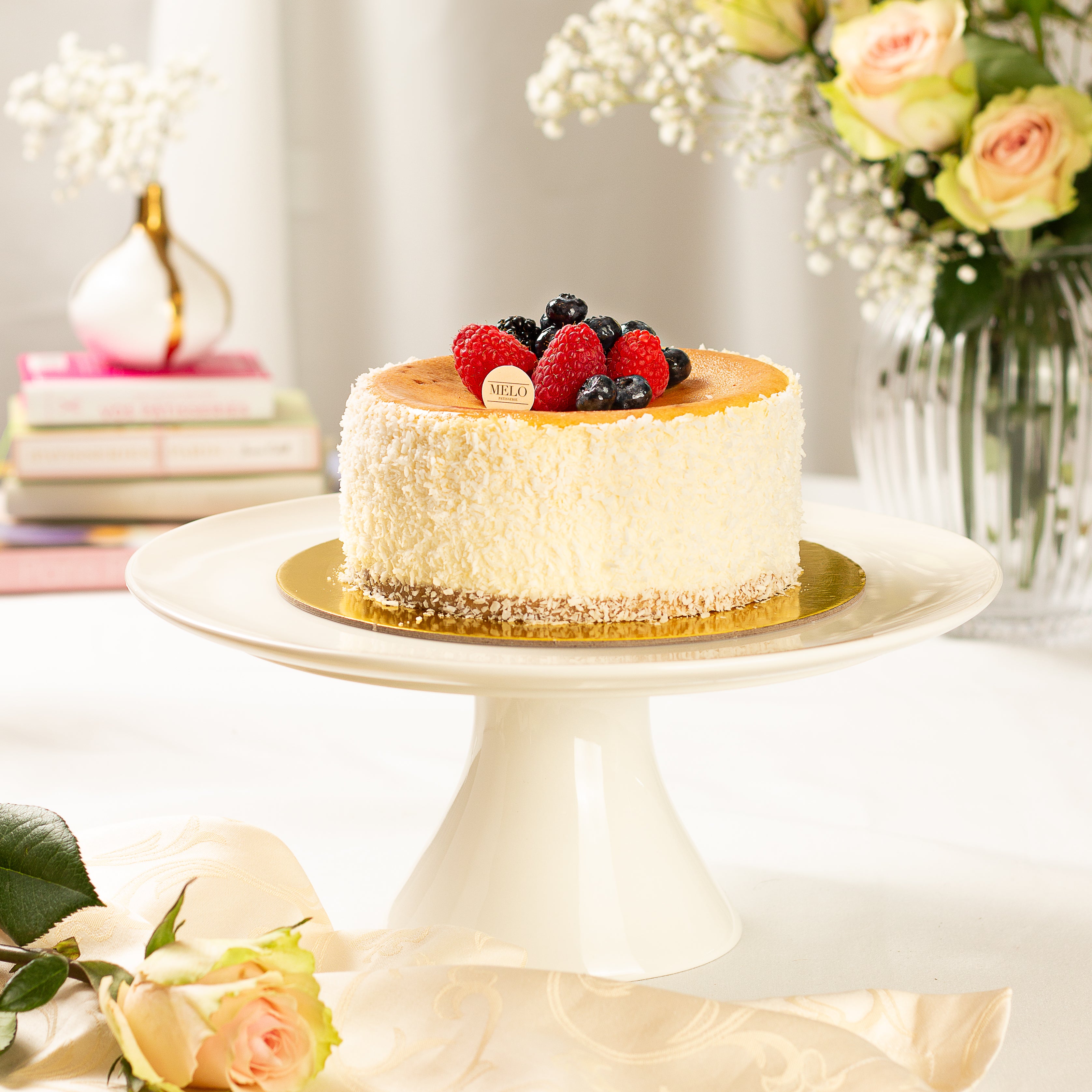 Cheesecake with berries on a white cake stand with flowers in the background