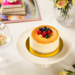 Small cake with berries on a white plate, surrounded by books and flowers