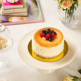 Small cake with berries on a white plate, surrounded by books and flowers