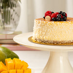 Decorative cake with berries on a white stand, surrounded by fruits.