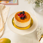 Small round cheesecake with berries on a white plate, surrounded by flowers and a book