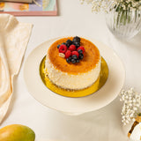 Small round cheesecake with berries on a white plate, surrounded by flowers and a book