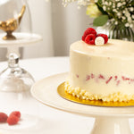 White cake with raspberries on a gold stand in a elegant setting