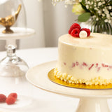 White cake with raspberries on a gold stand in a elegant setting