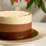 Chocolate mousse cake on a white plate with flowers in the background