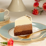 Layered dessert on a decorative plate with a cup and flowers in the background