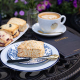 Scone on a plate with a cup of coffee and flowers on a table outdoors