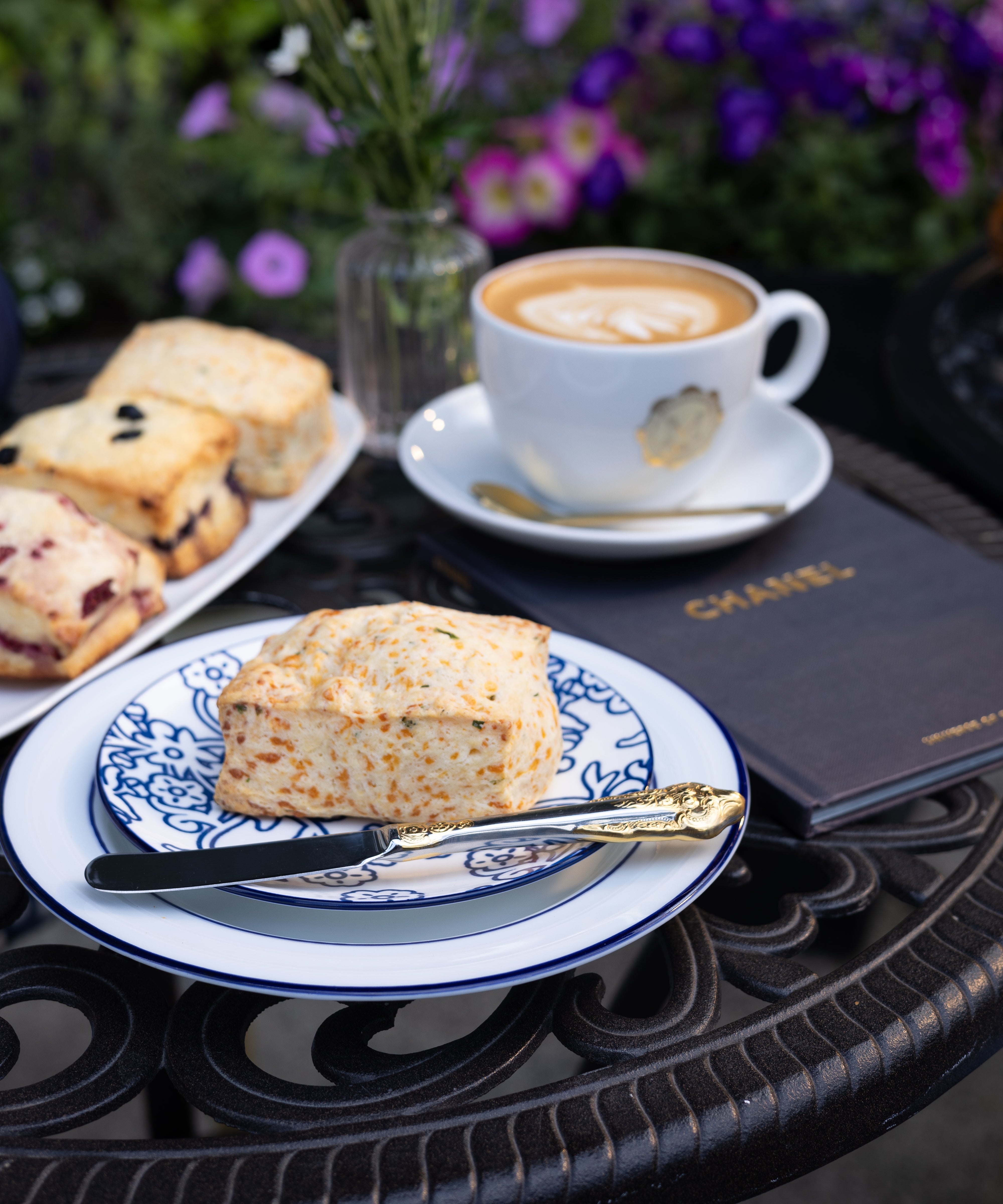 Scone on a plate with a cup of coffee and flowers on a table outdoors