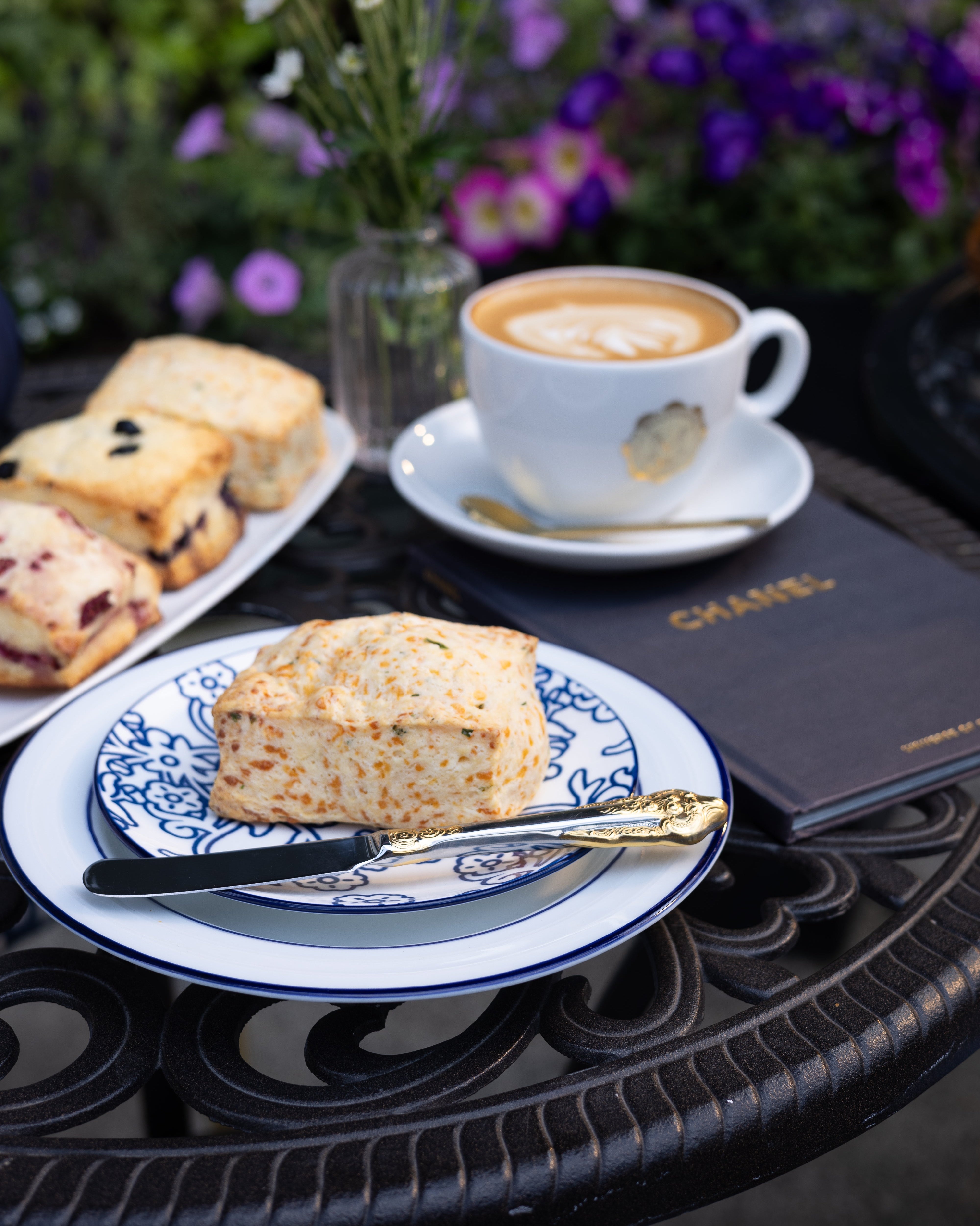 Scone on a plate with a cup of coffee and flowers on a table outdoors