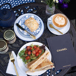Outdoor setting with a meal, coffee, and Chanel book on a table.