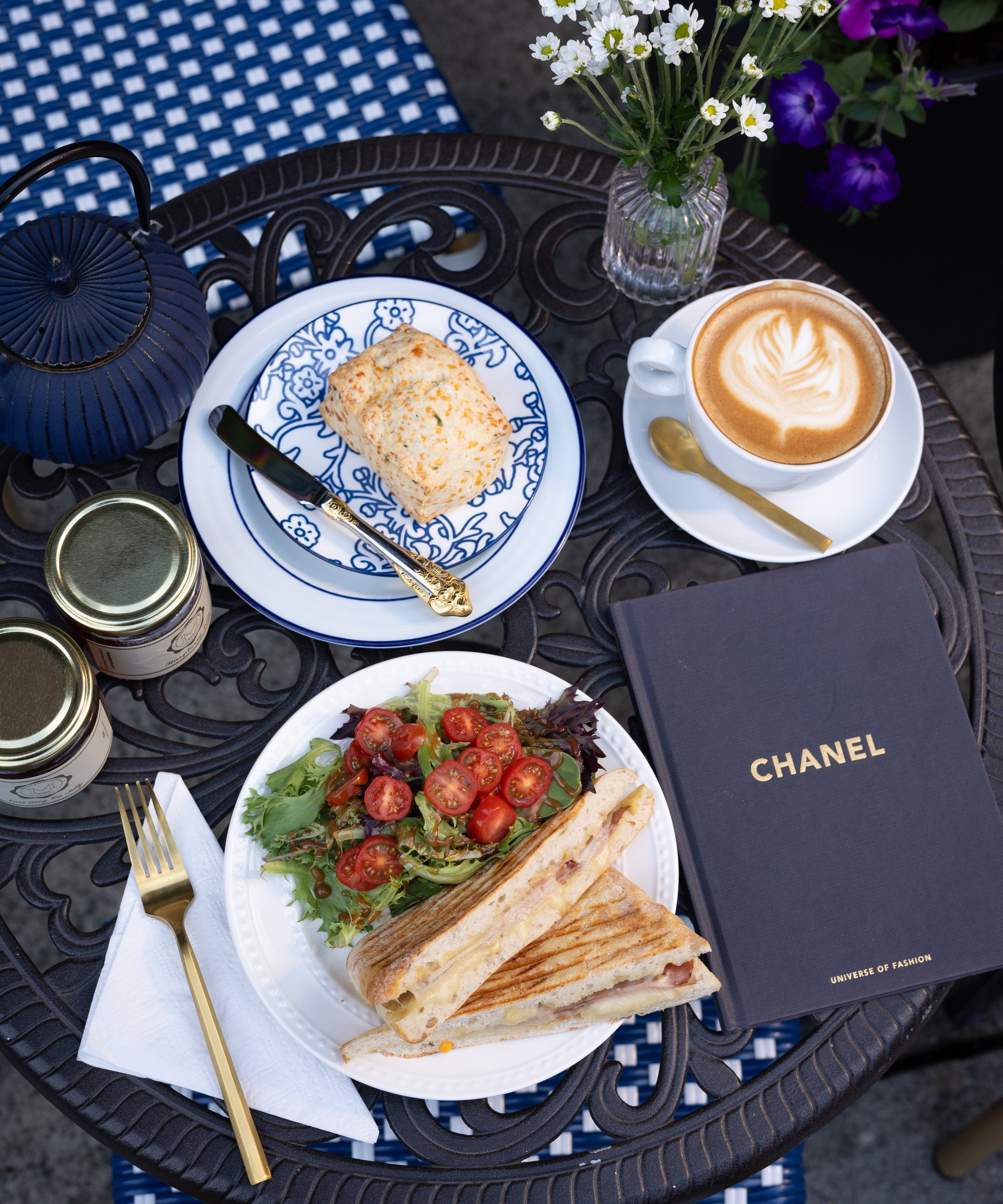Outdoor setting with a meal, coffee, and Chanel book on a table.