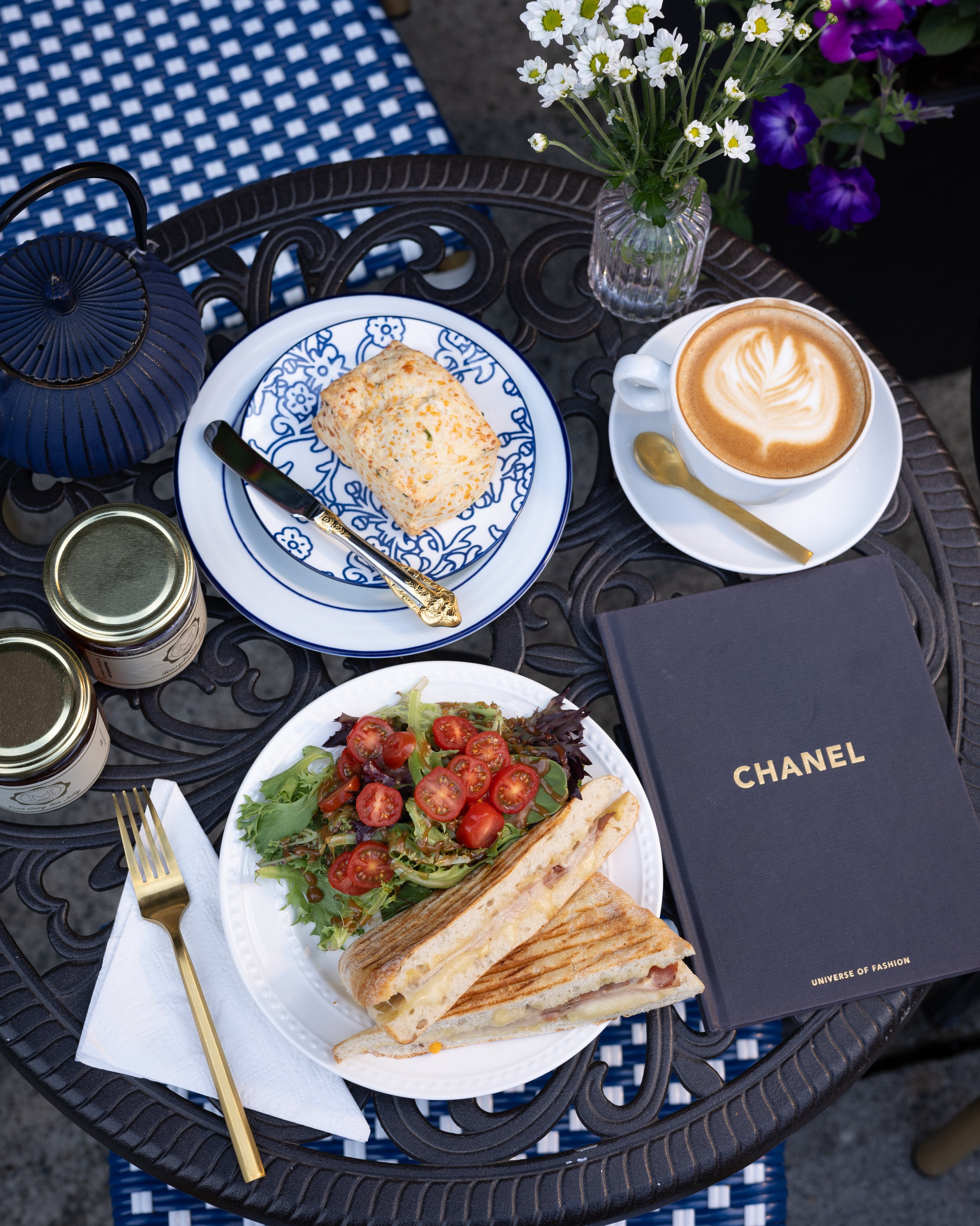 Outdoor setting with a meal, coffee, and Chanel book on a table.