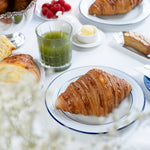 Table with croissants, raspberries, and a glass of green juice on a white tablecloth.