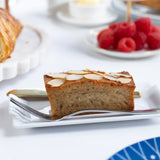 Slice of almond financier cake on a plate with raspberries and a teacup in the background