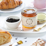 Jar of earl grey tea jelly, croissant, and cake on a white table with a blurred background