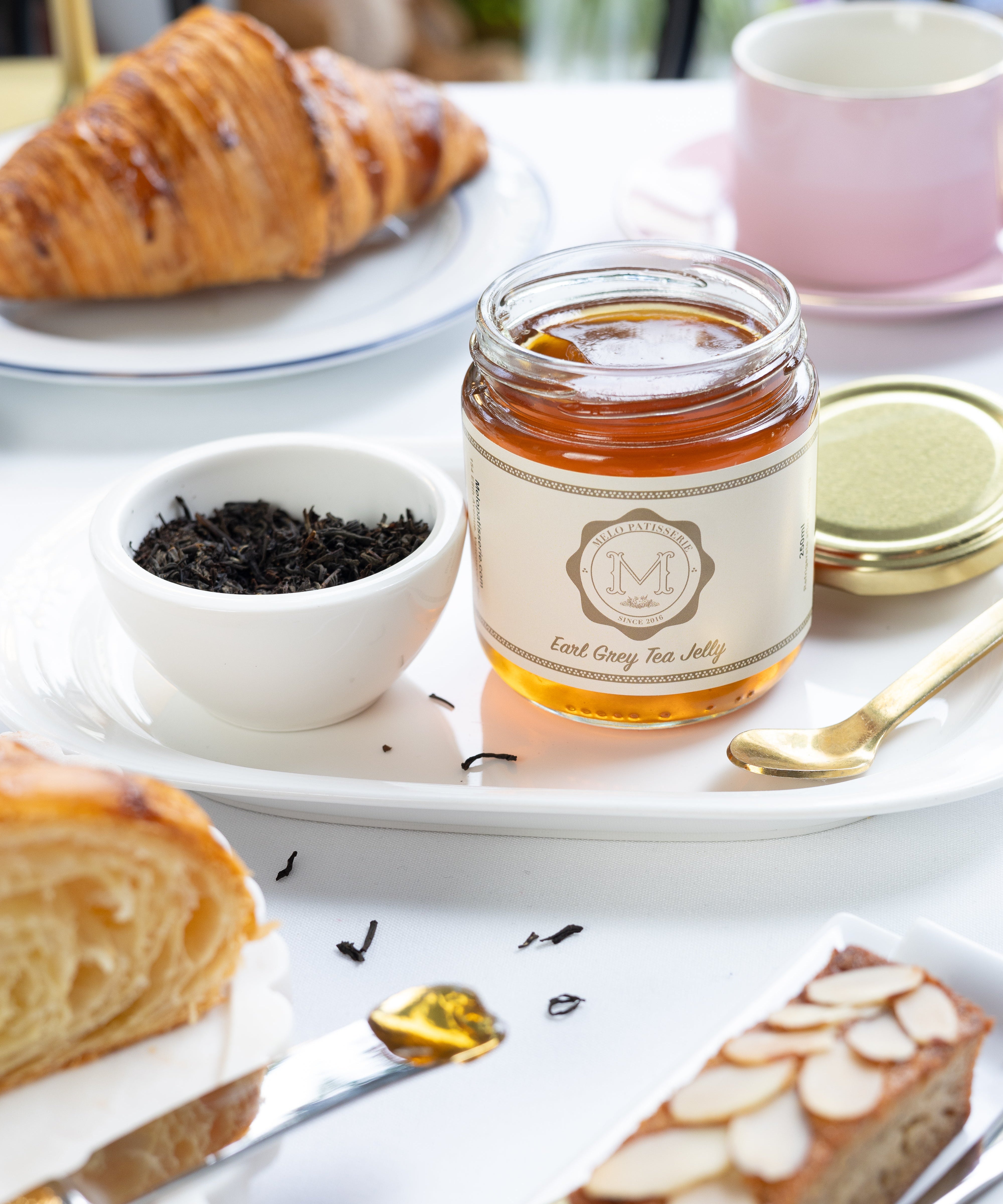 Jar of earl grey tea jelly, croissant, and cake on a white table with a blurred background