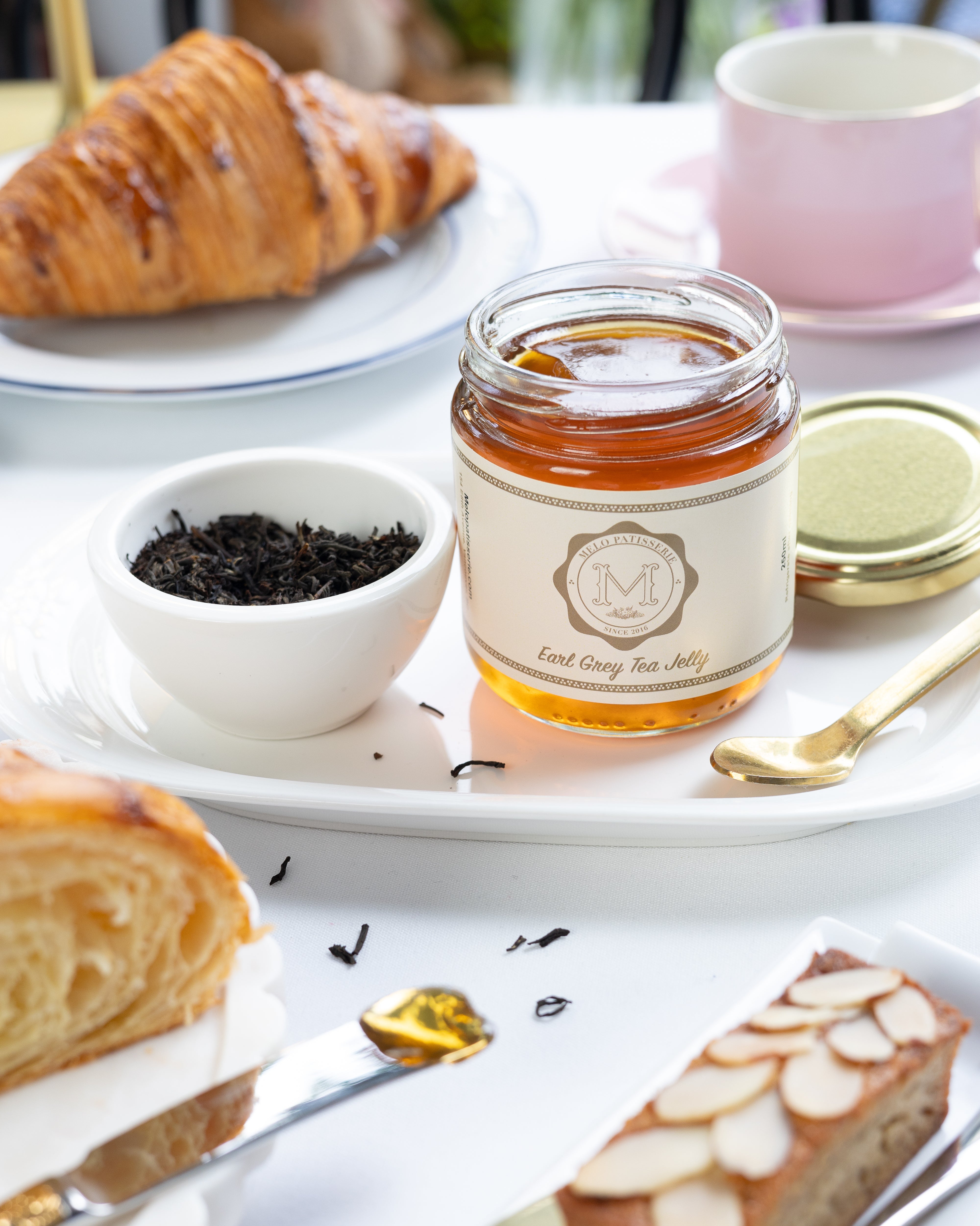 Jar of earl grey tea jelly, croissant, and cake on a white table with a blurred background