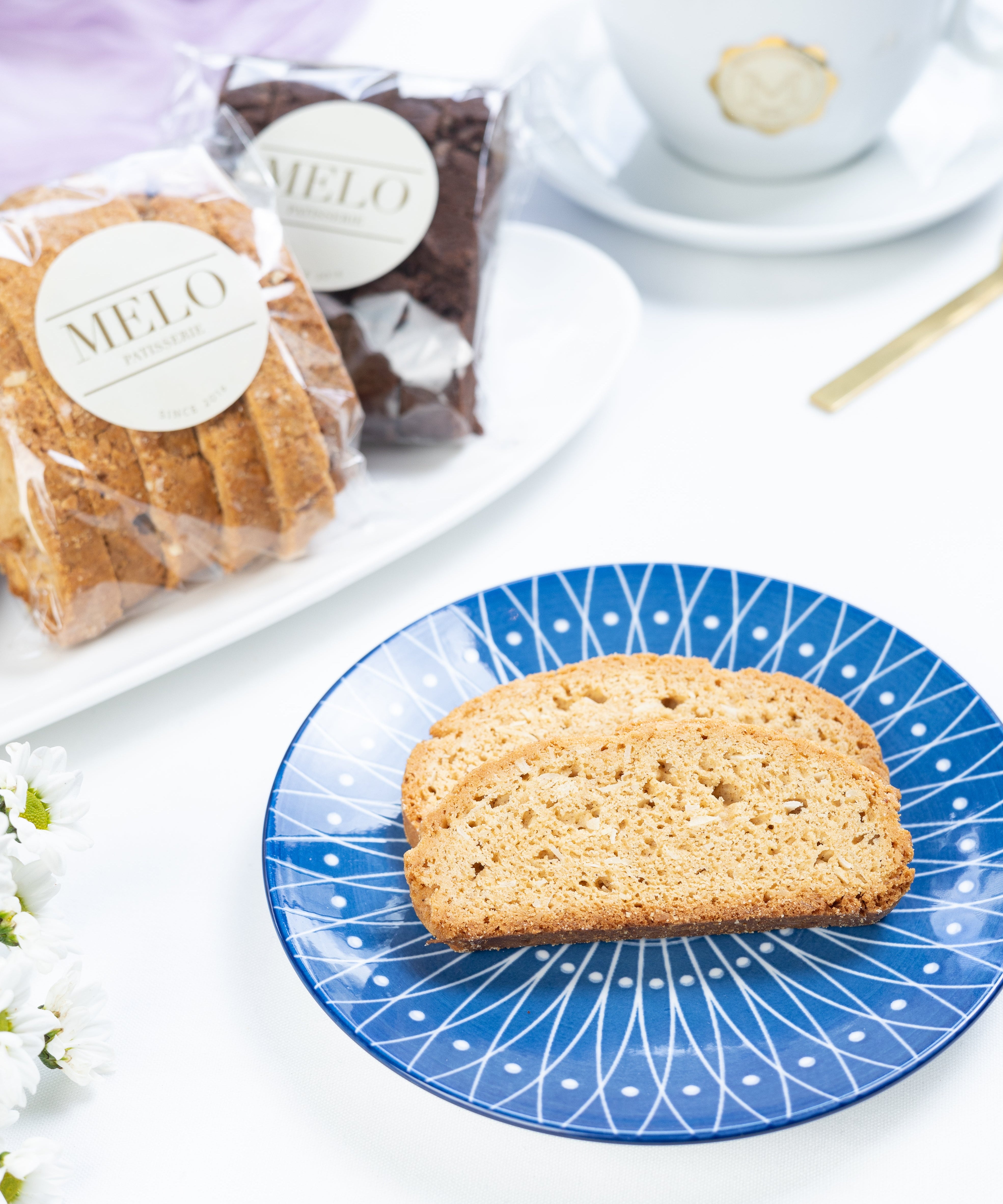Biscotti on a blue plate with a cup of coffee and packaged pastries in the background.